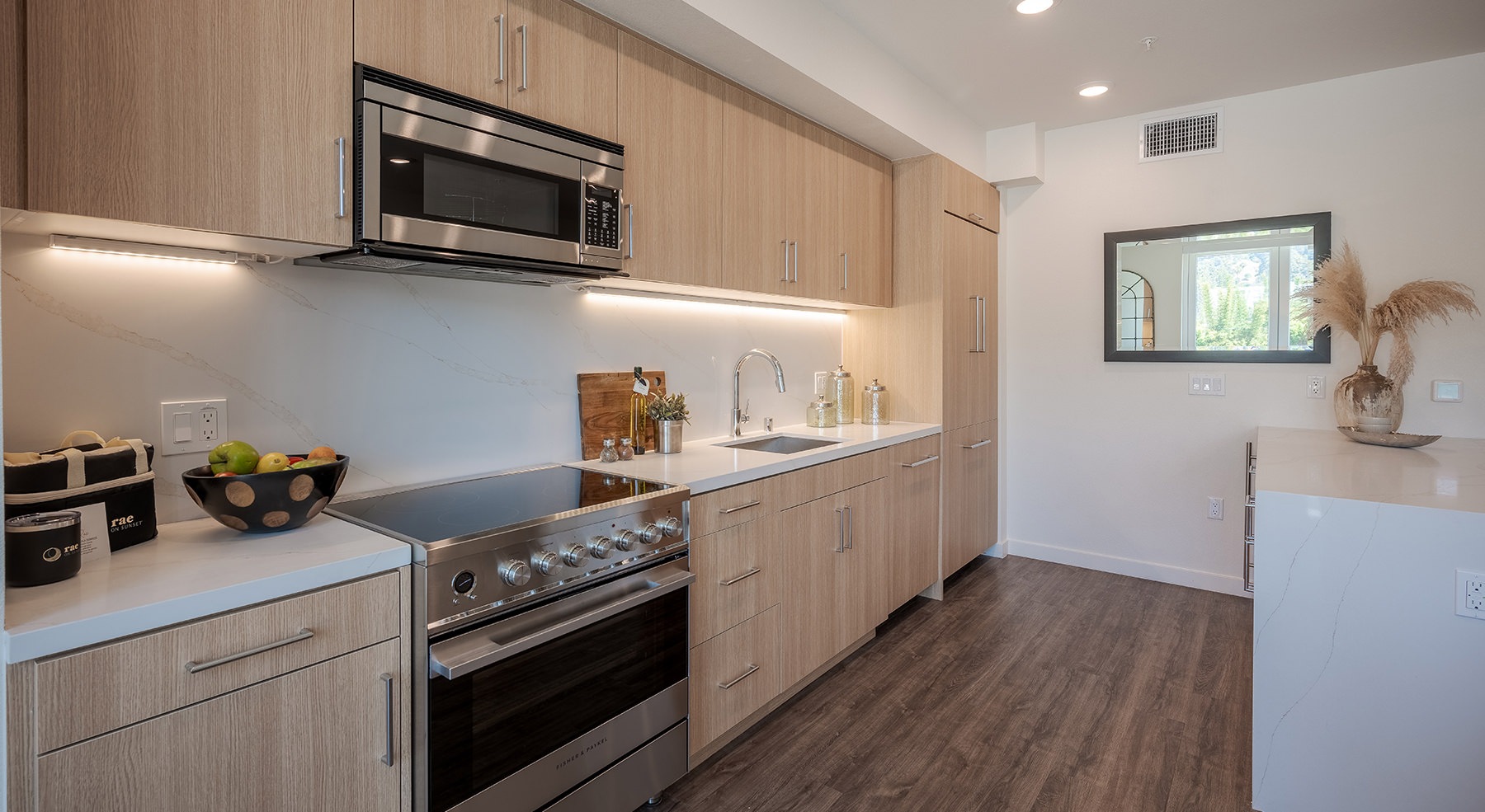 A spacious kitchen with ample cabinetry, a long kitchen island, and dining area at a penthouse apartment in Rae on Sunset.